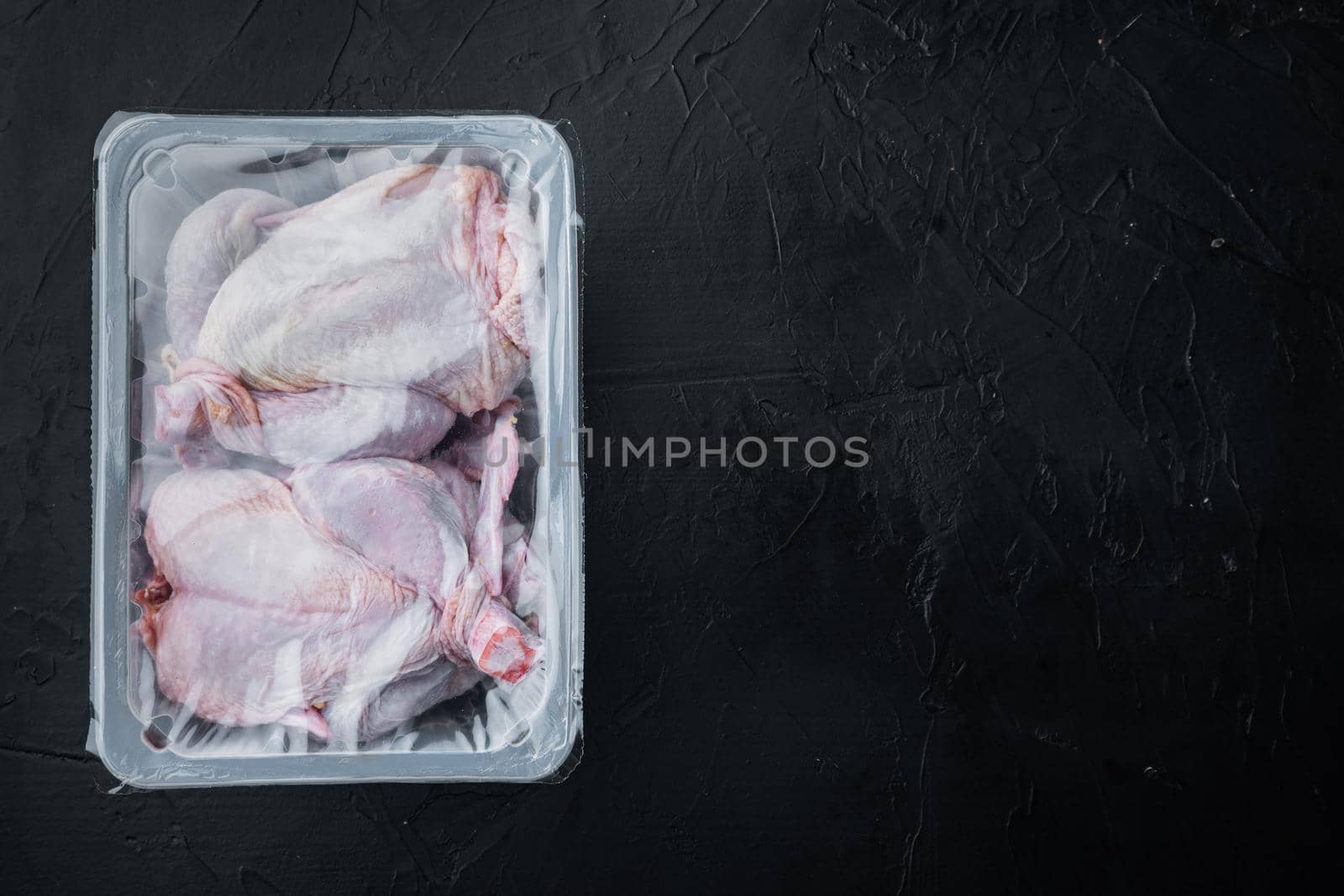 Raw chicken set in plastic vacuum tray, on black background, top view with copy space for text