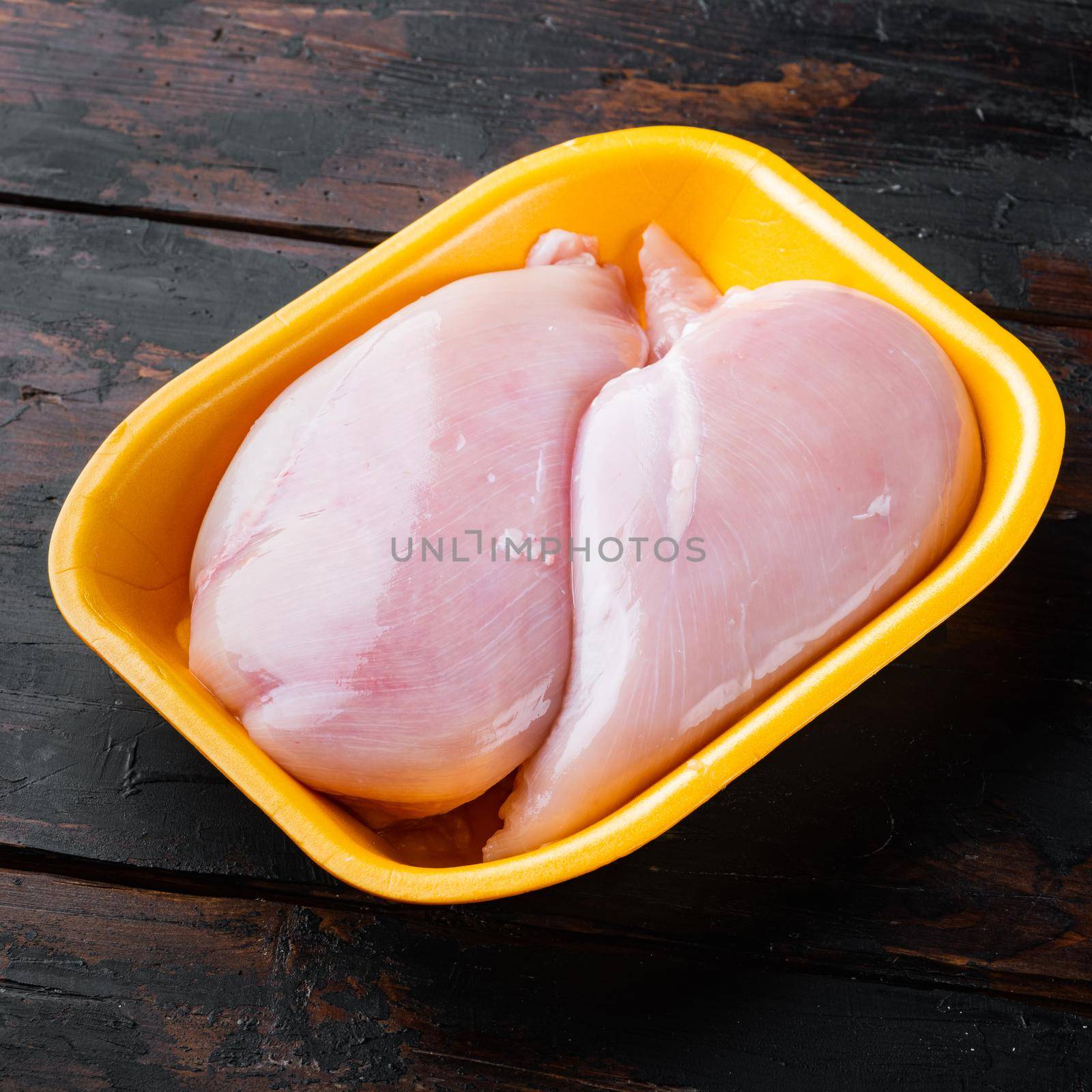 Raw chicken breast fillets in tray, on dark wooden background