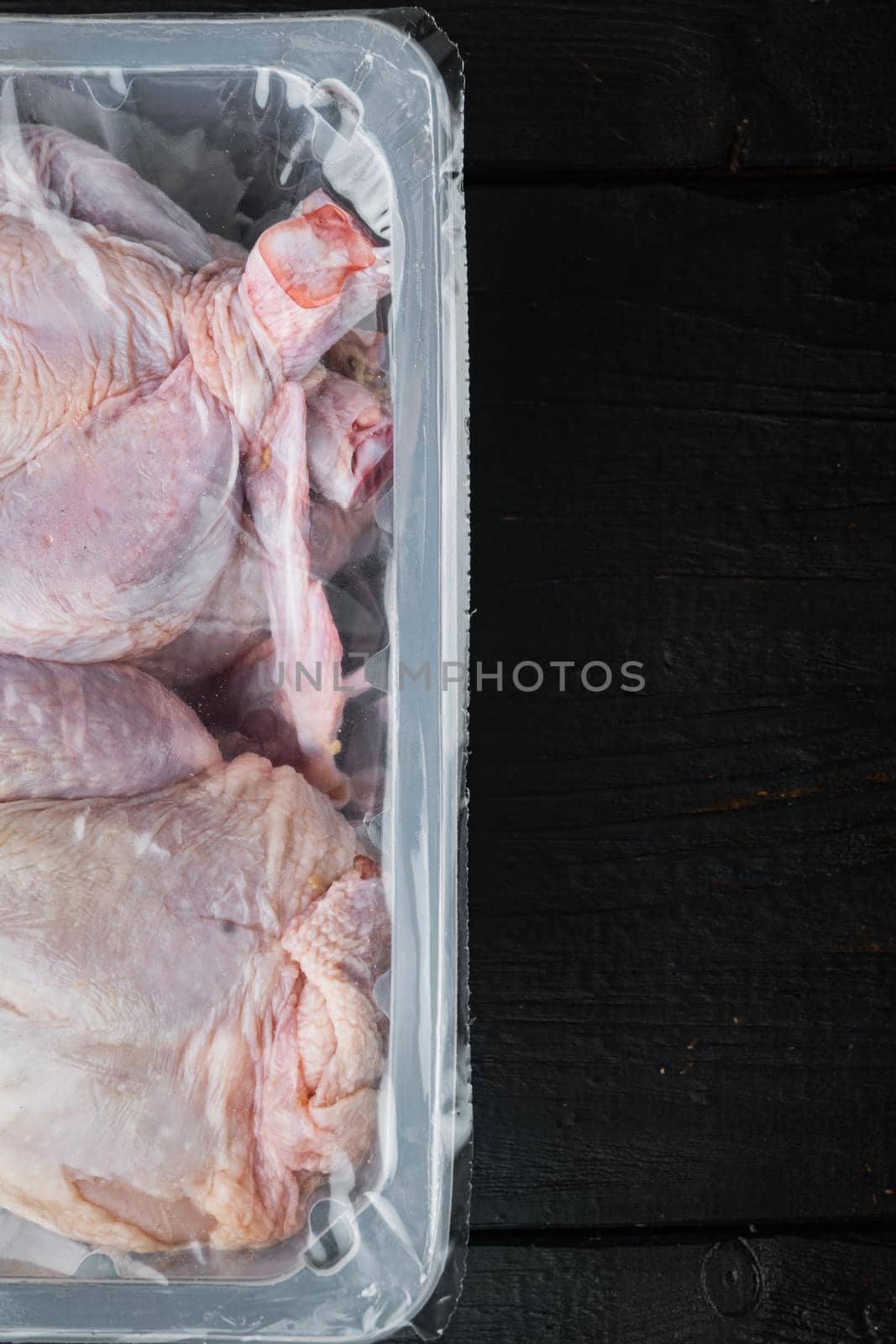 Raw chicken in plastic sealed plastic box, on black wooden table, top view with copy space for text