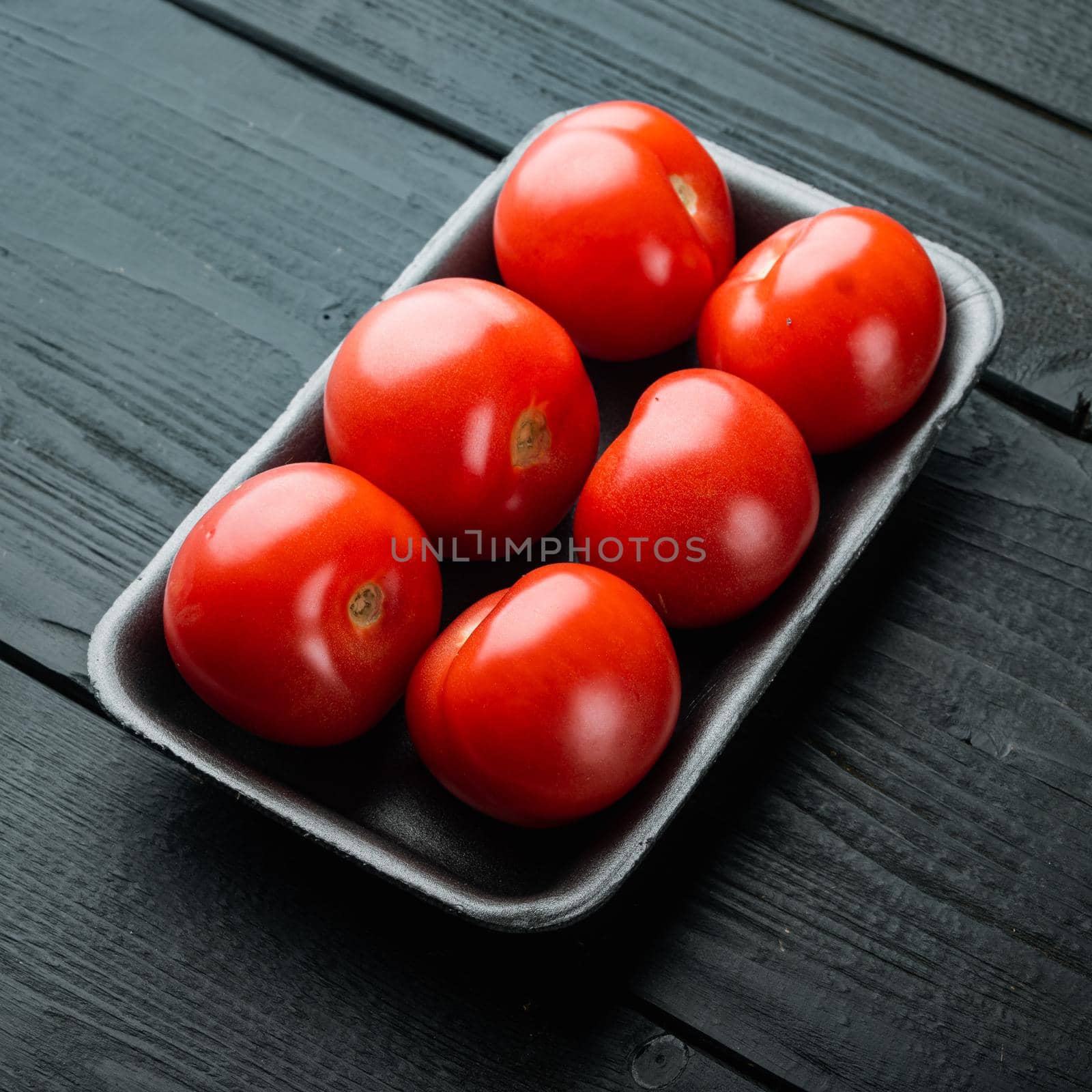 Red ripe tomatoe, on black wooden table by Ilianesolenyi