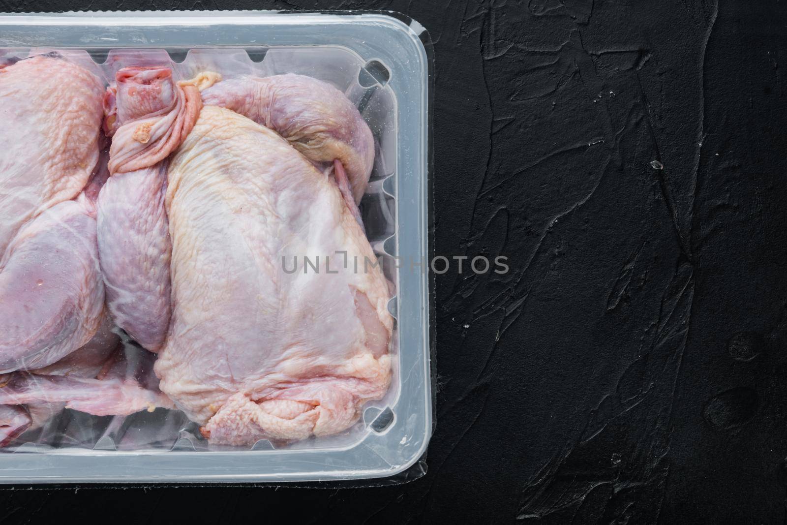 Raw chicken set in plastic vacuum tray, on black background, top view with copy space for text
