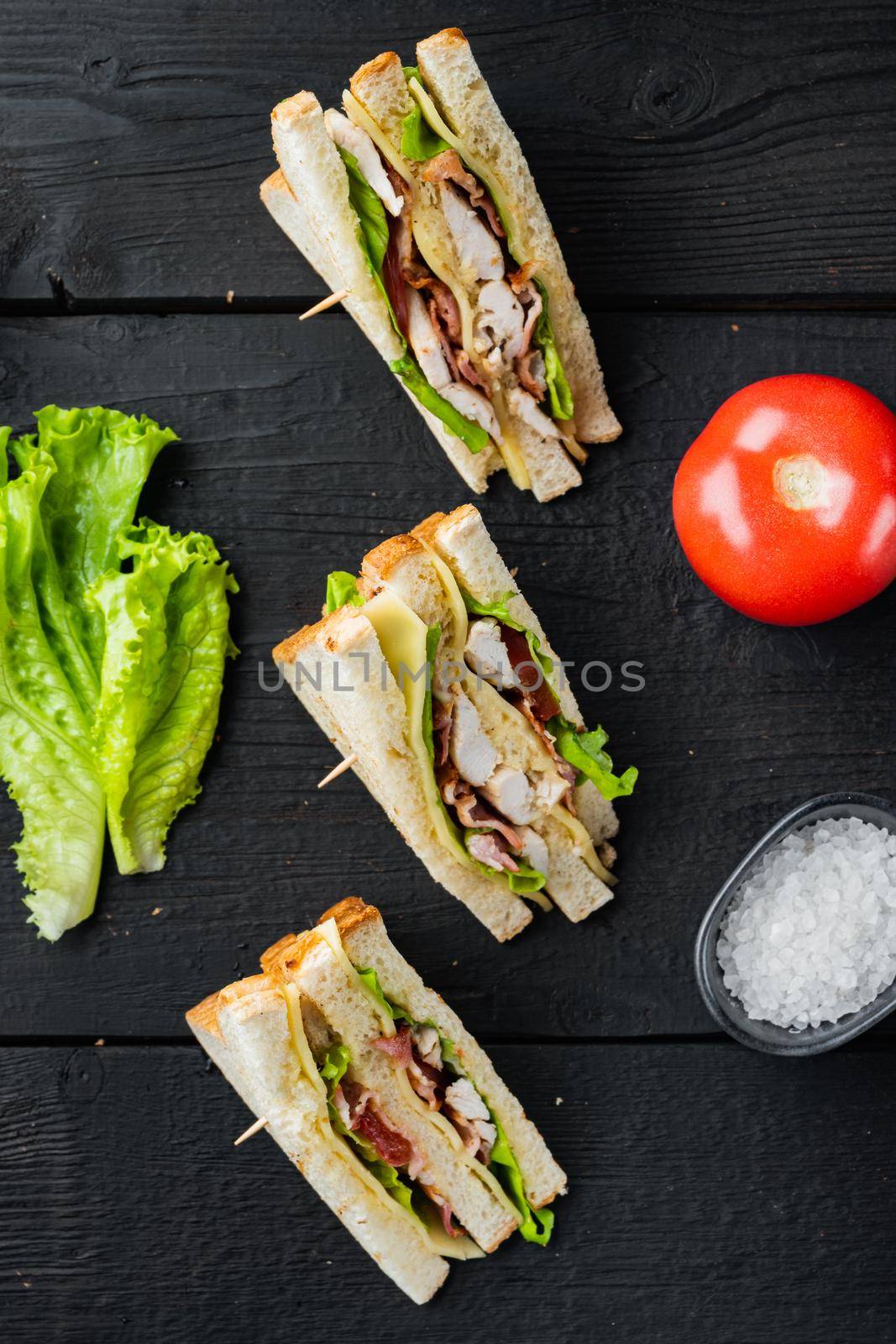 Homemade chicken sandwich halves, on black wooden background, top view