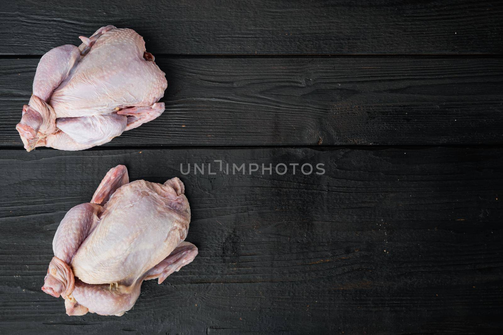 Raw small young whole chicken, on black wooden background, top view with copy space for text