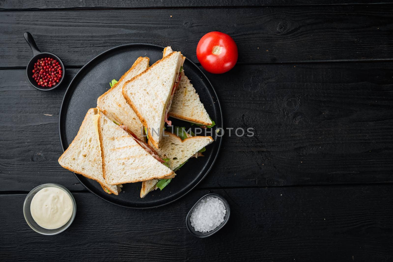 Sandwich with ham, cheese, tomatoe, lettuce, chicken meat and toasted bread, on black wooden background, top view with copy space for text