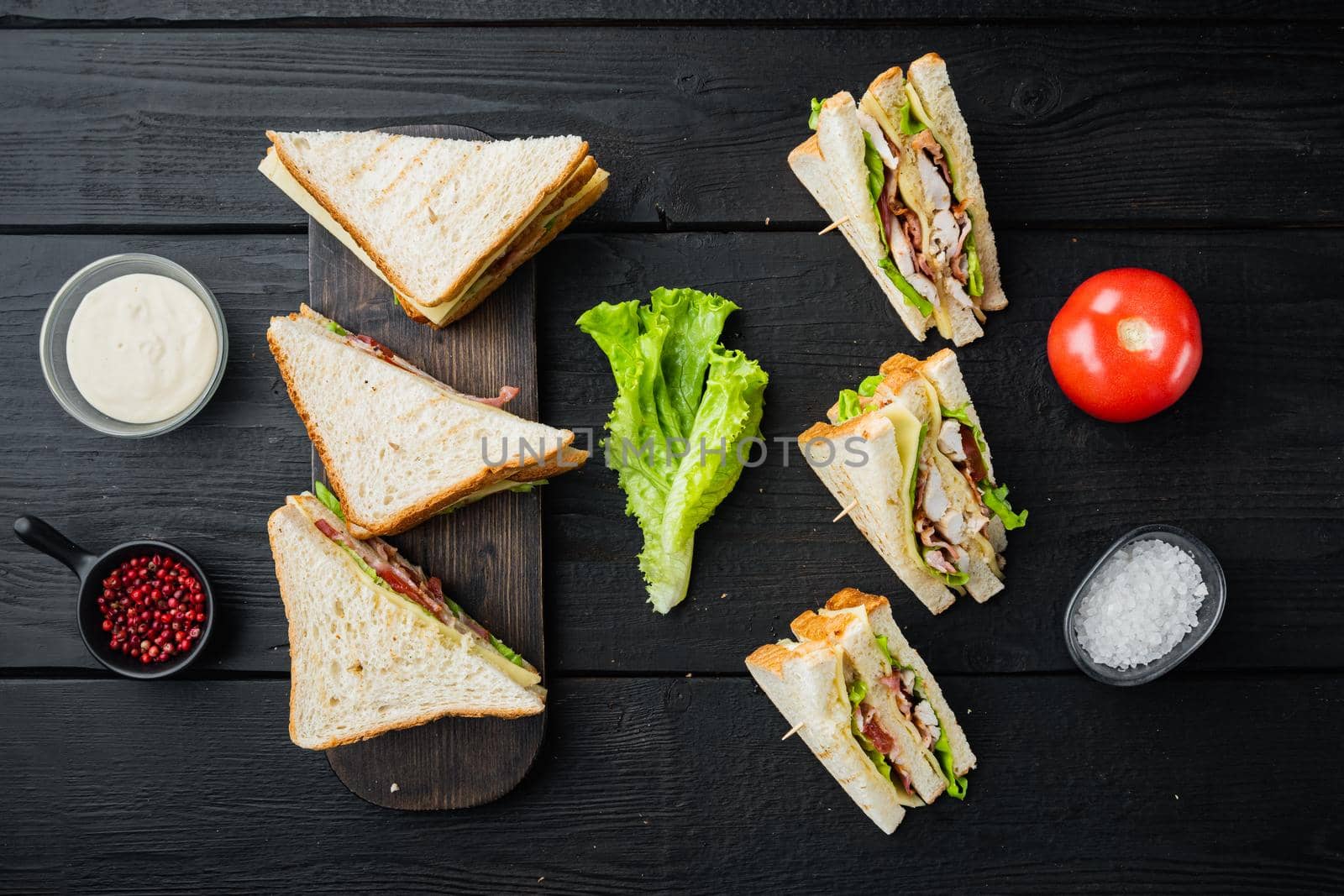 Homemade club sandwich made with turkey, bacon, ham, tomatoes, on black wooden background, top view