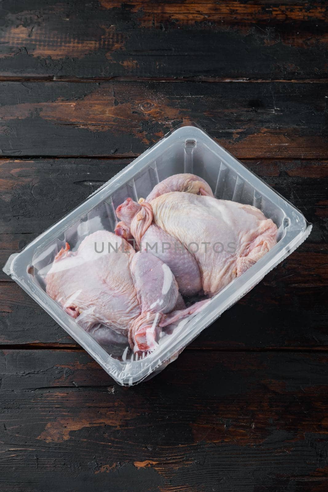 Plastic container with raw chicken set, on old wooden table, on black wooden background with copy space for text