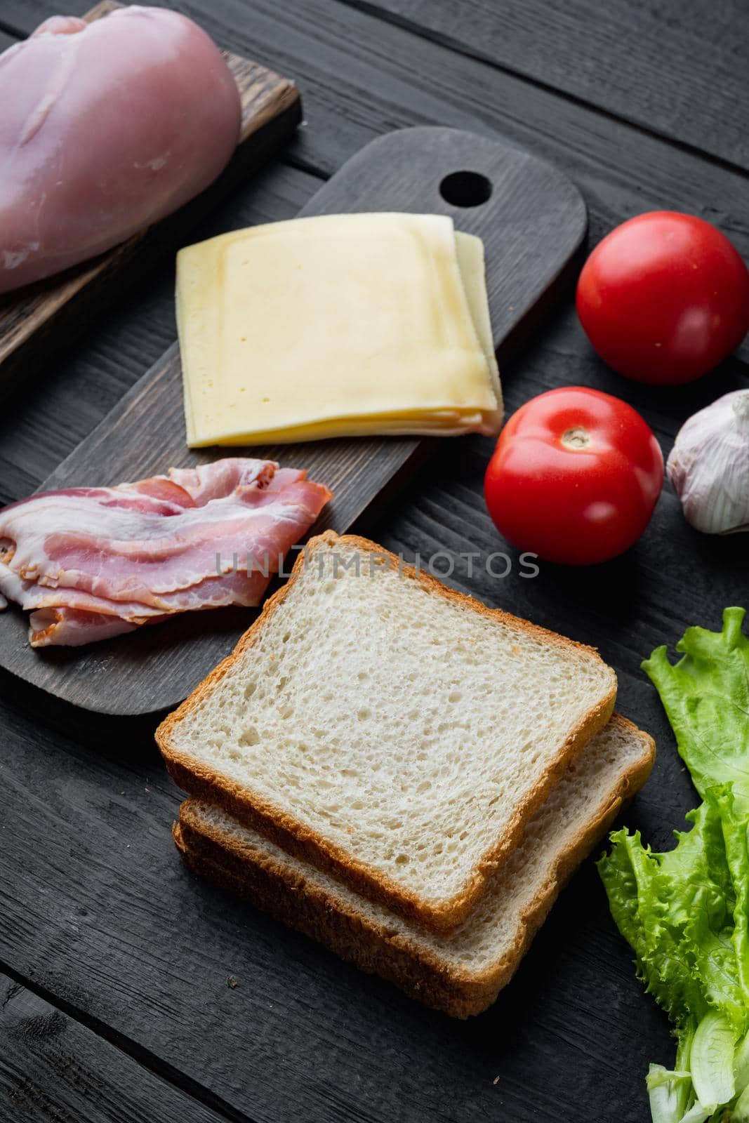 Ingredients for sandwich, bacon, cheese, tomato, chicken meat, lettuce, sauce, on black wooden table