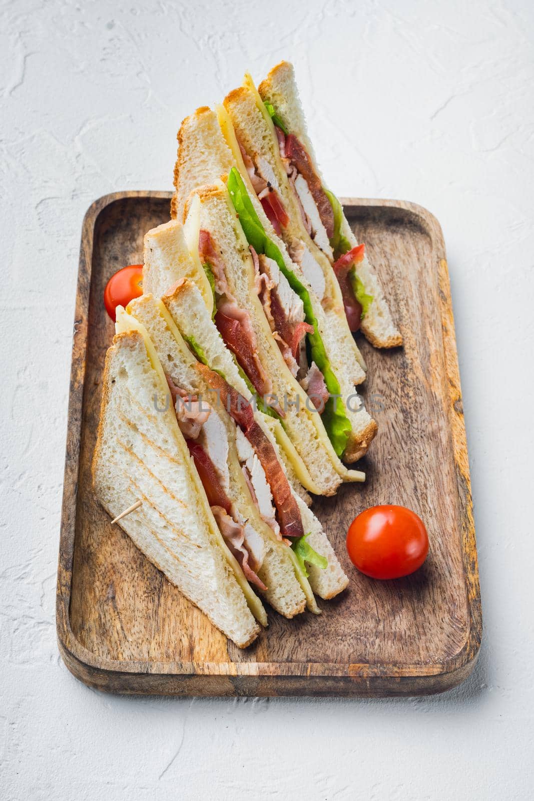 Homemade club sandwich made with turkey, bacon, ham, tomatoes, on white background