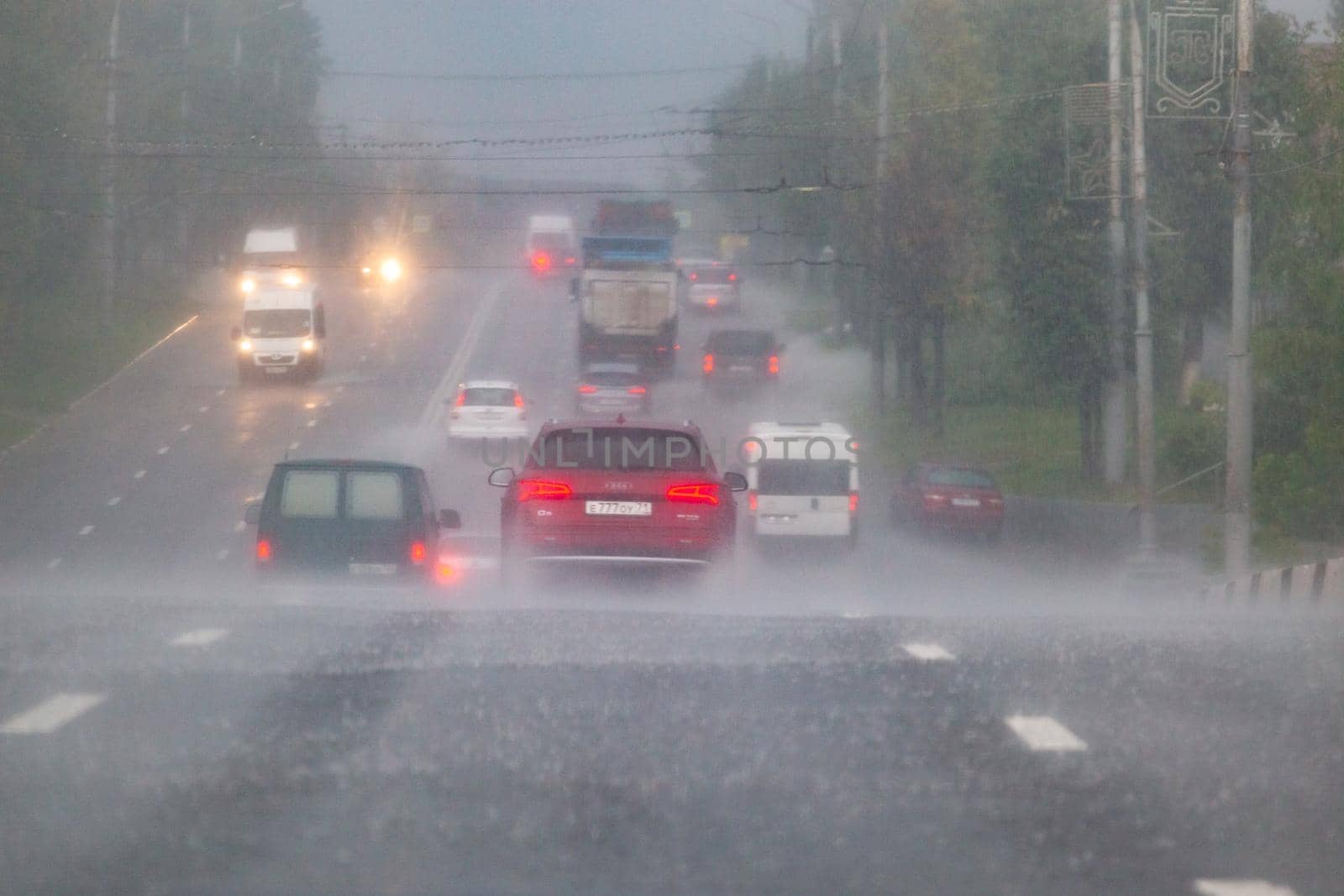 TULA, RUSSIA - JULY 14, 2020: Cars moving on asphalt road during heavy summer storm rain, back view from another car on same road. Water spraying from the wheels.