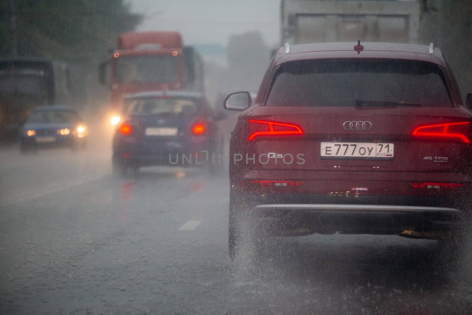 TULA, RUSSIA - JULY 14, 2020: Cars moving on asphalt road during heavy summer storm rain, back view from another car on same road. Water spraying from the wheels.