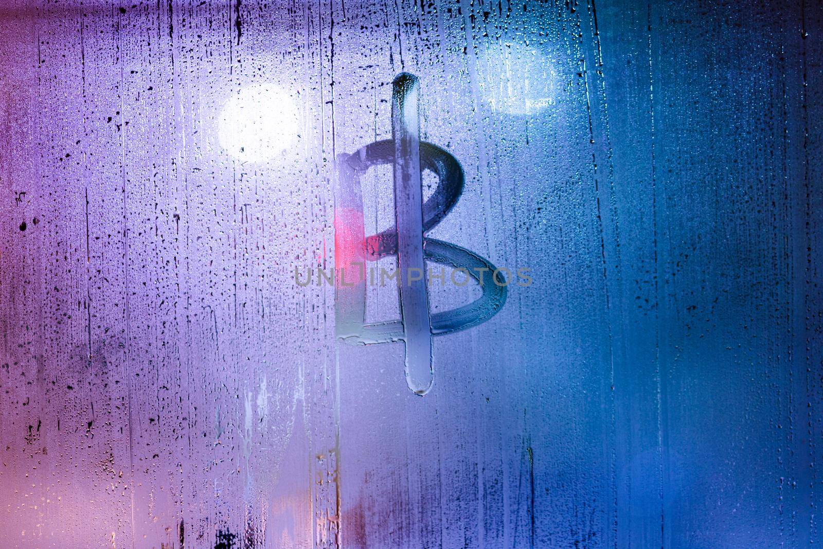 bitcoin symbol - handwritten on wet glass of night window, close-up with selective focus and background blur