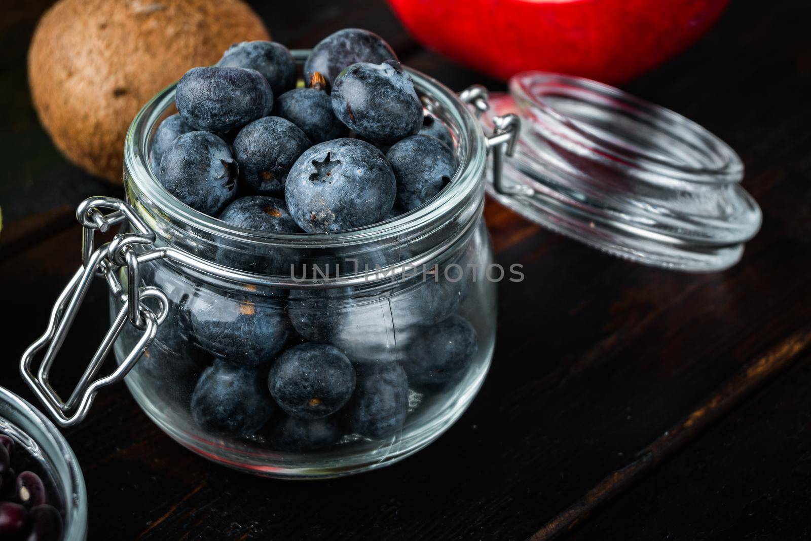 Ripe blueberry in glass jar on dark wooden background.