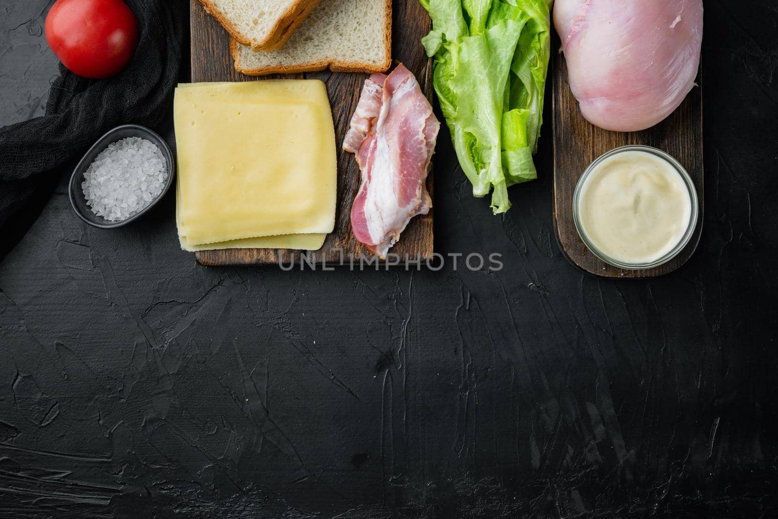 Ingredients for sandwich, bacon, cheese, tomato, chicken meat, lettuce, sauce, on black background, top view with copy space for text