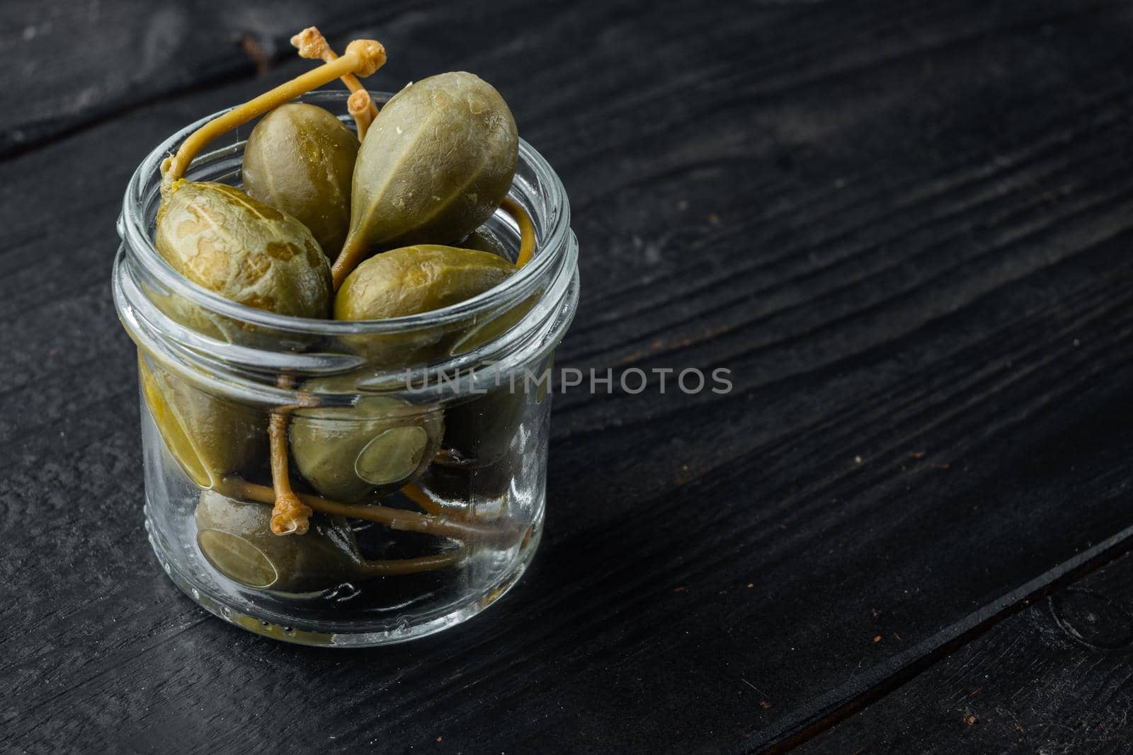 Capers, marinated in oil, on black wooden background with copy space for text
