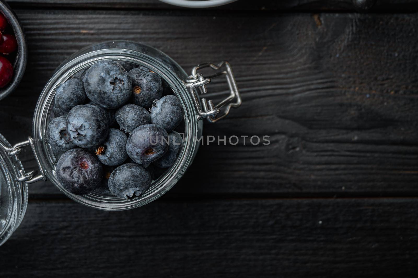 Ripe blueberry in glass jar, flat lay with space for text, on black wooden background.