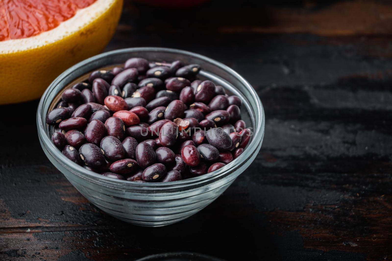 Red beans in bowl with healthy ingredients on dark wooden background, with space for text.
