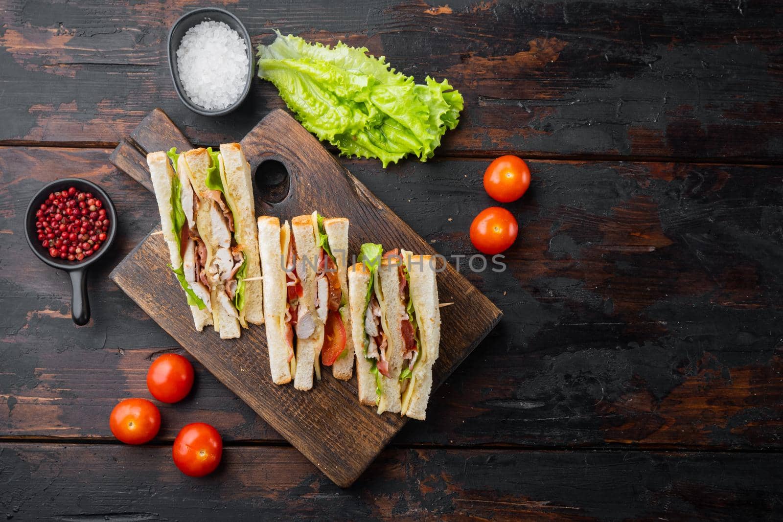 Homemade club sandwich made with turkey, bacon, ham, tomatoes, on old wooden table, top view with copy space for text