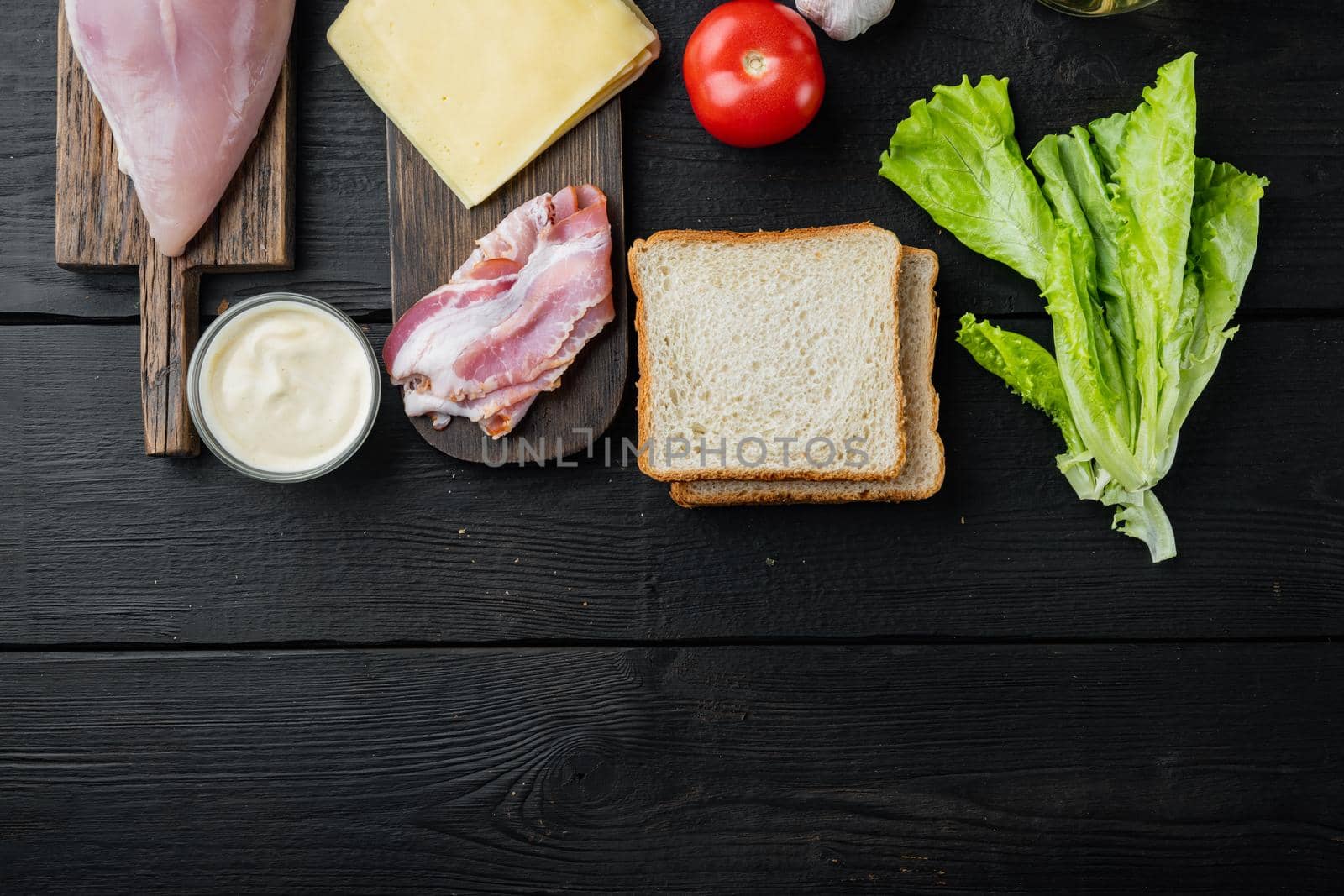 Ingredients for sandwich, bacon, cheese, tomato, chicken meat, lettuce, sauce, on black wooden background, top view with copy space for text