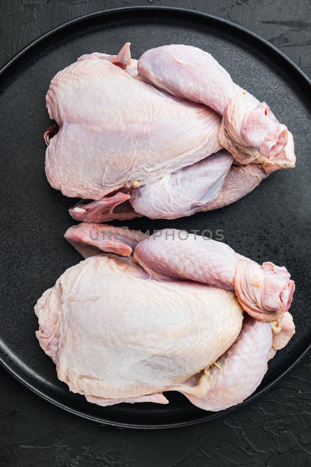 Raw organic uncooked whole chicken meat, on black background, top view