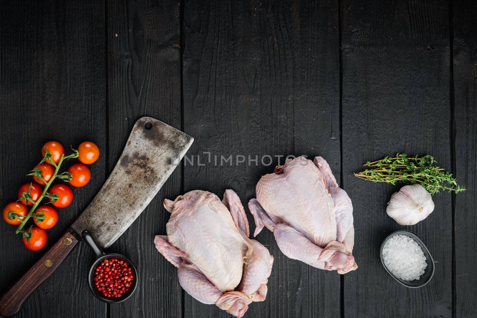 Raw small young whole chicken with herbs spices, on black wooden background, top view with copy space for text