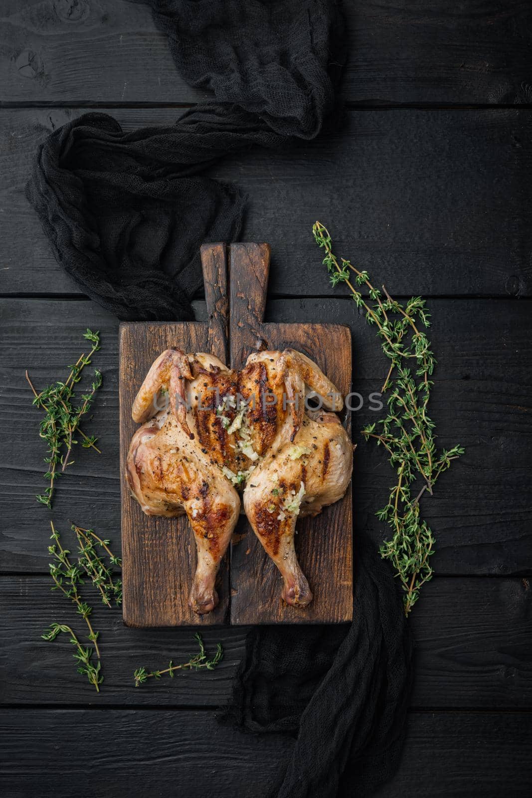 Roasted whole poussins, on black wooden background, top view