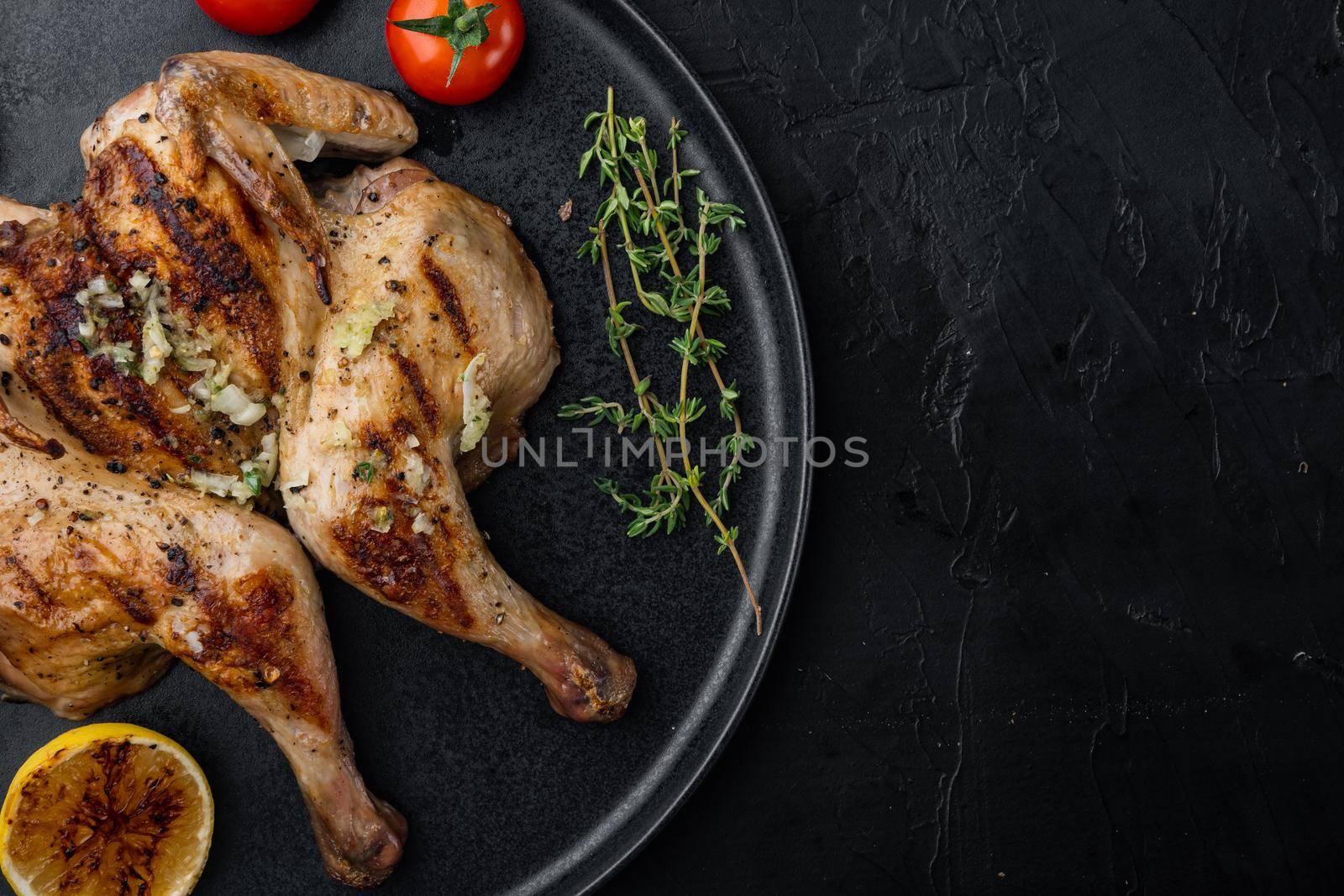 Spatchcocked chicken and herbs, on black background, top view with copy space for text