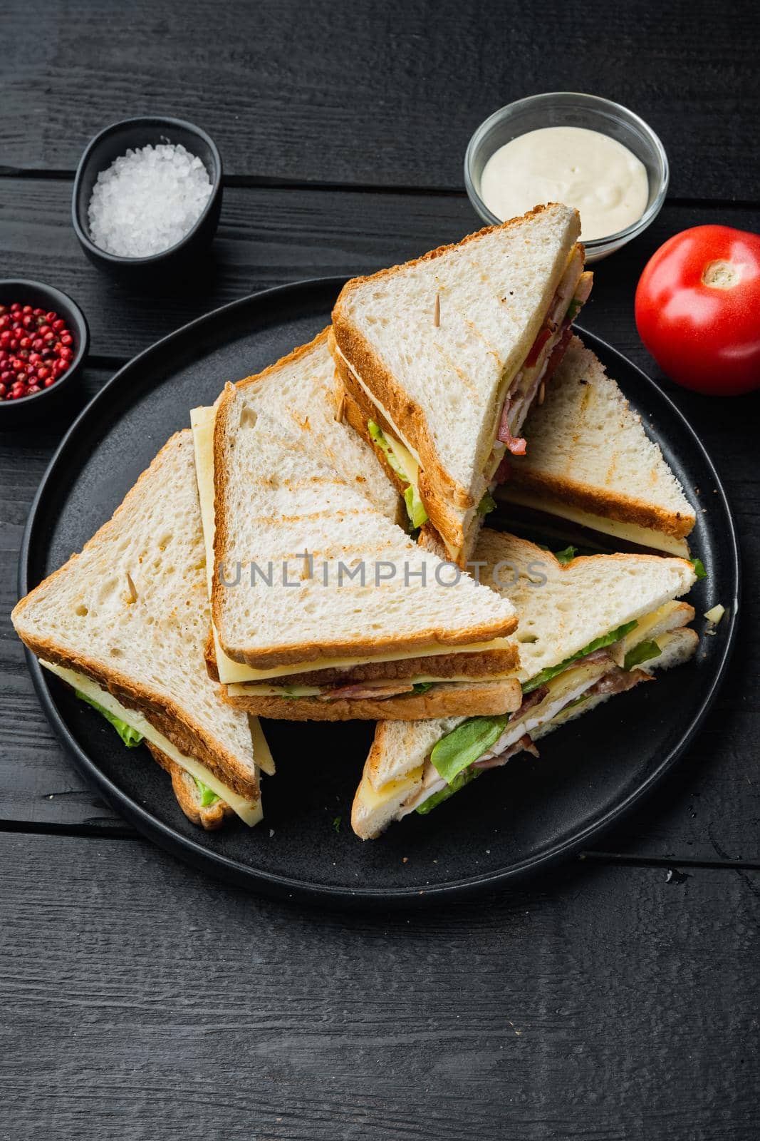 Club sandwich with meat, cheese tomato, ham, on black wooden table