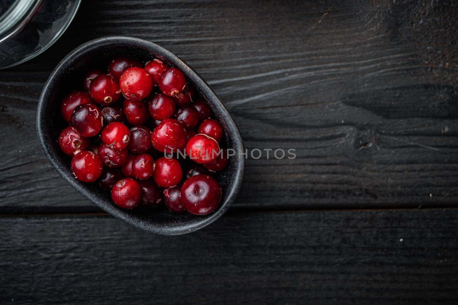 Cranberry, ripe red berry in bowl, flat lay with space for text, on black wooden background.