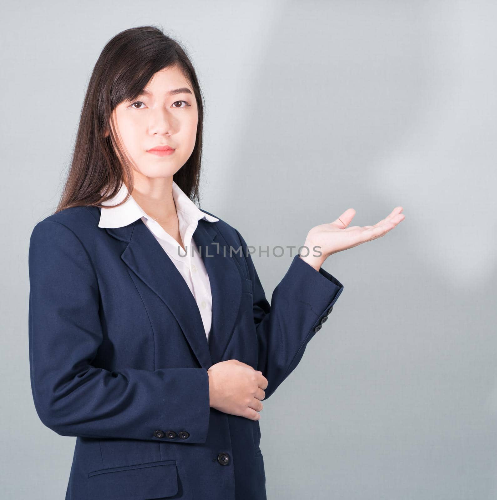 Asian woman in suit open hand palm gestures with empty space on gray background