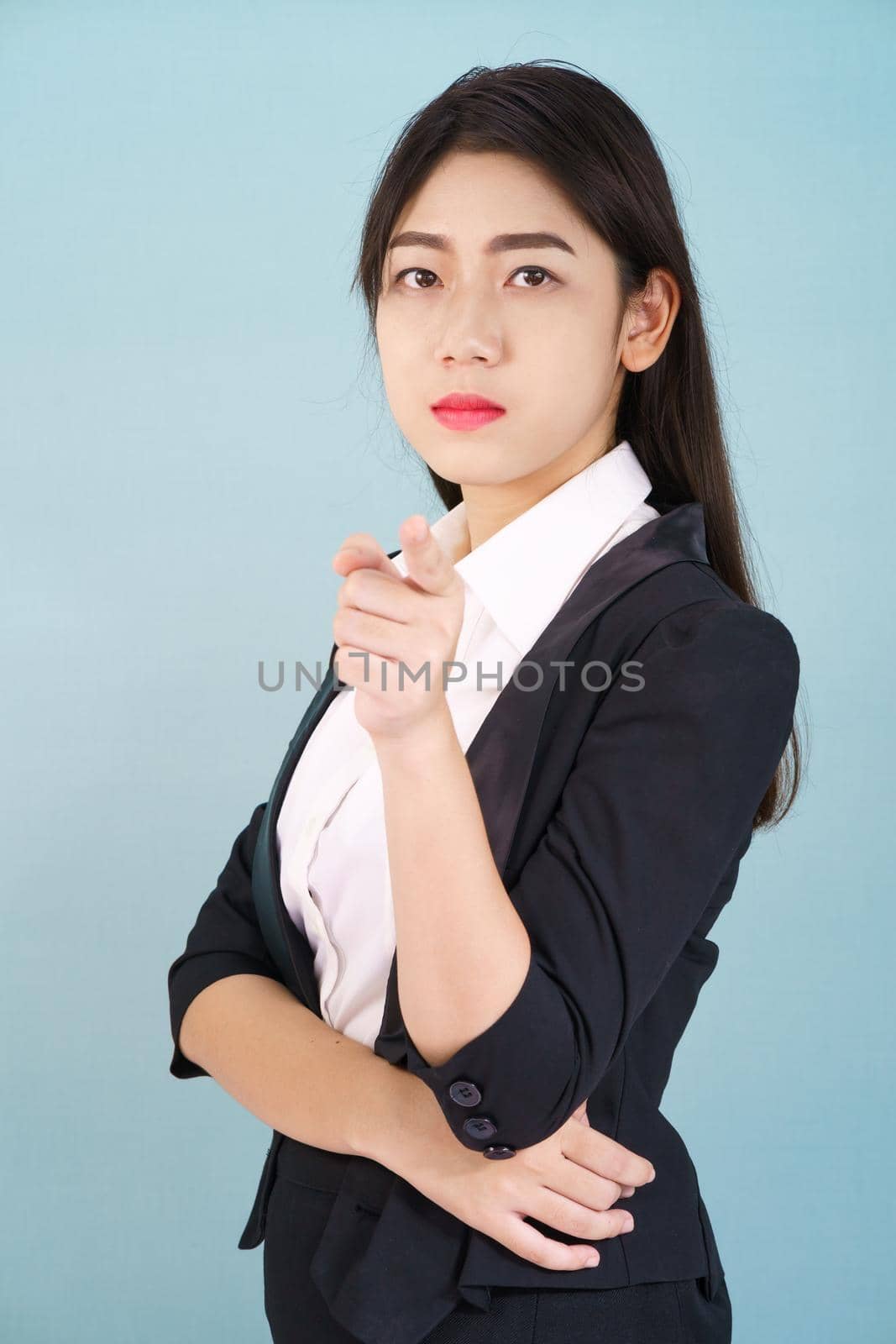 Asian woman looking at camera and pointing finger on blue background