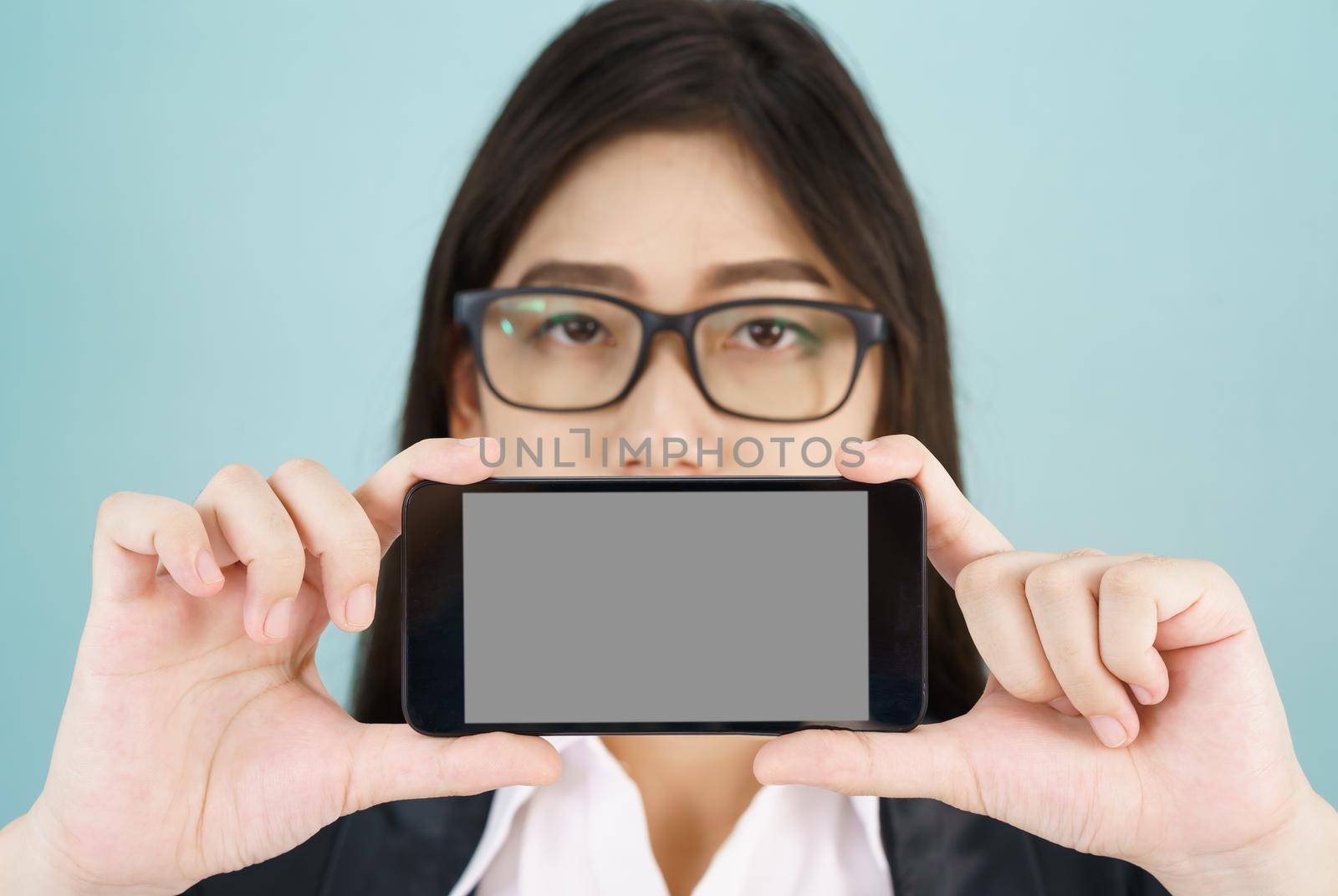 Young women in suit holding her smartphone standing against blue background