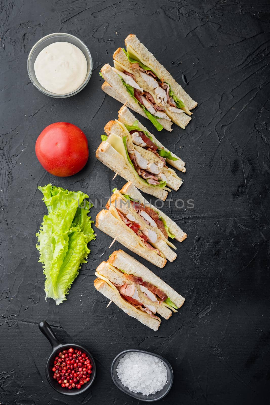 Halves of fresh club sandwiches, on black background, top view
