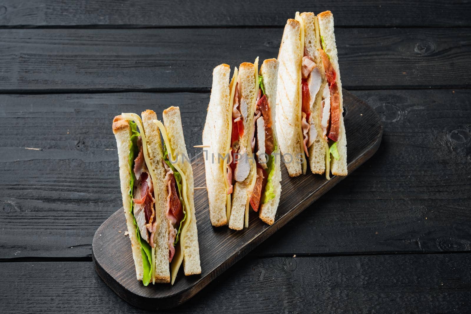 Sandwich bread tomato lettuce and yellow cheese, on black wooden table
