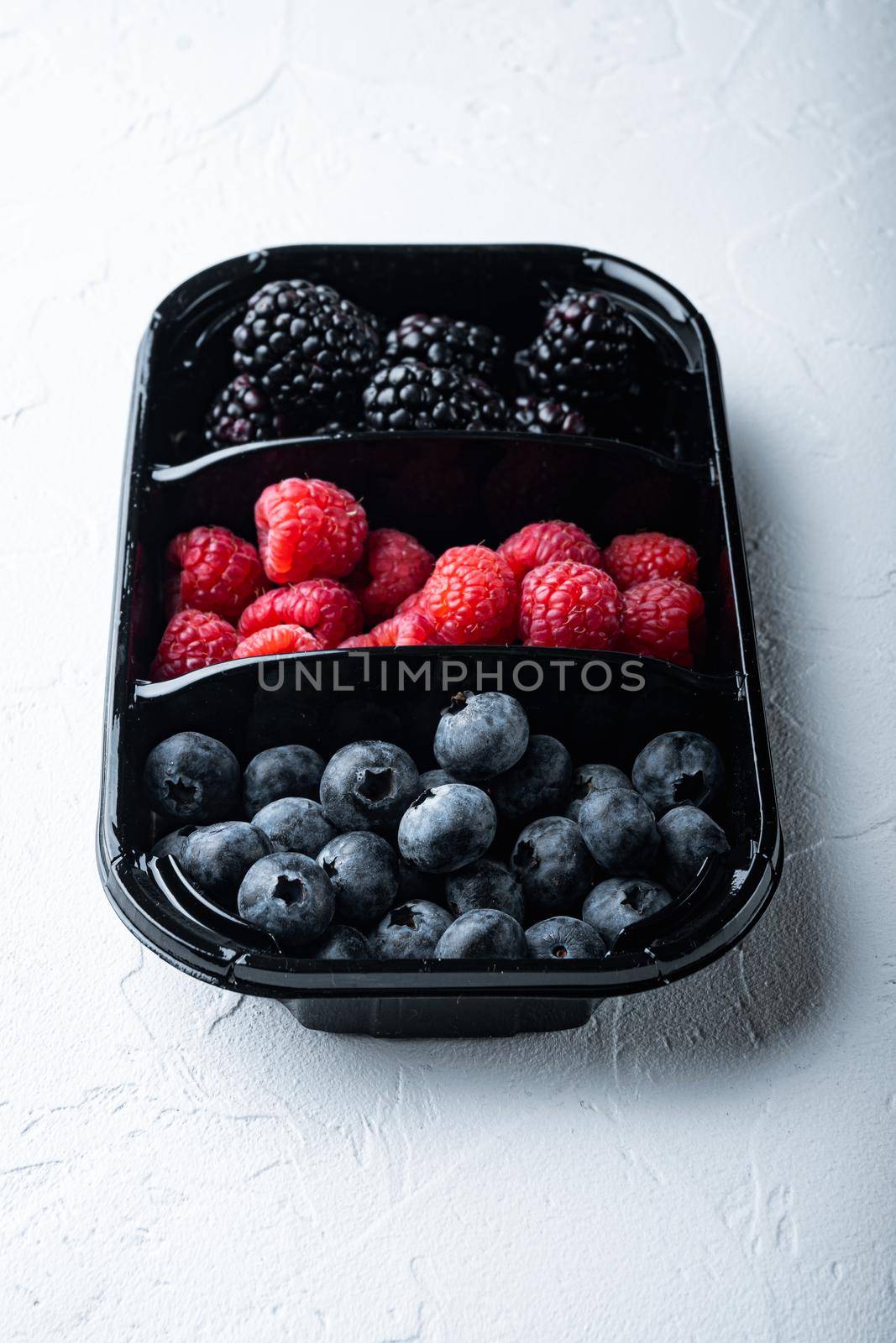 Ripe berries in tray from market, blueberries, raspberry with blackberry, on white background