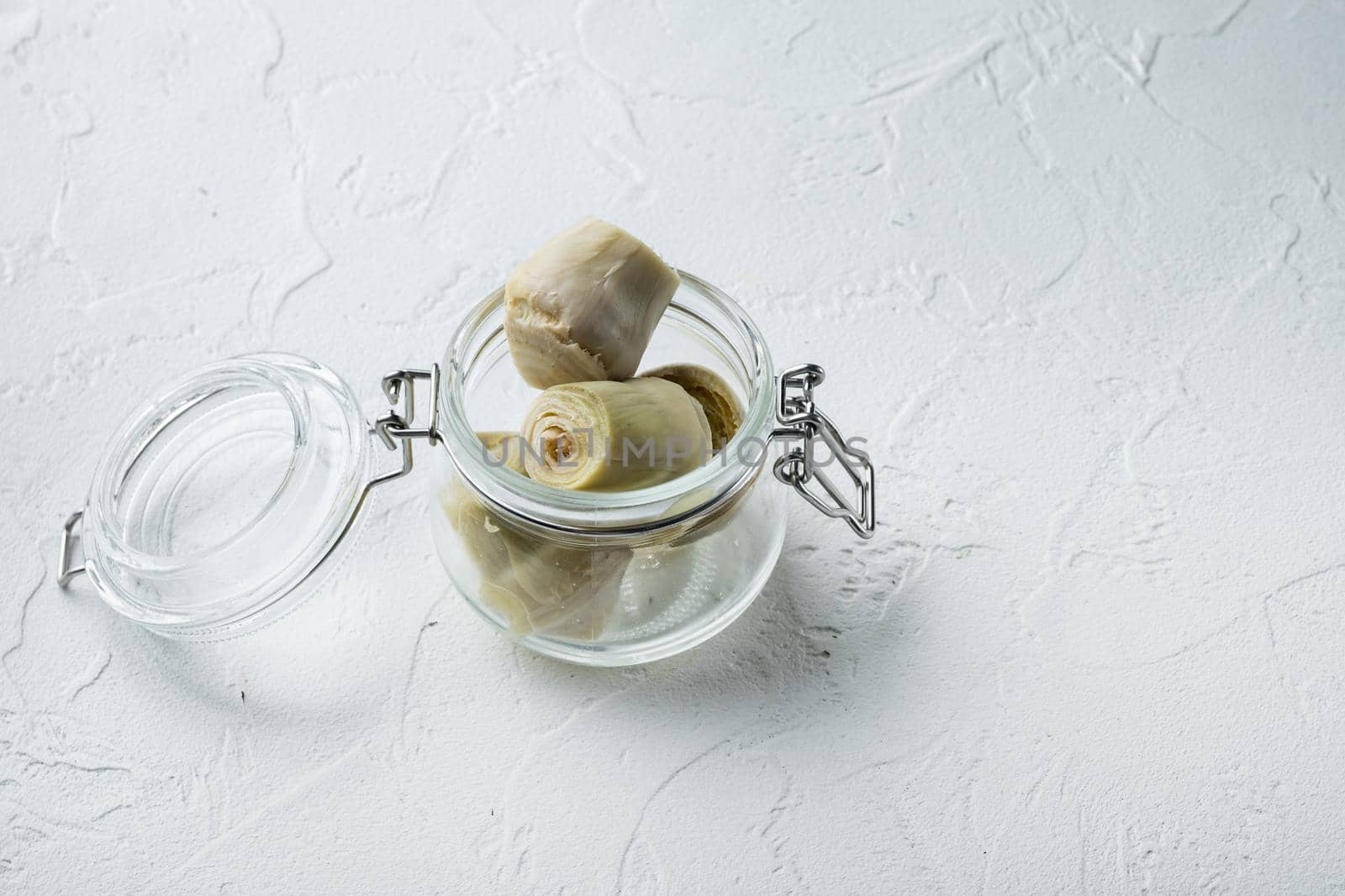 Artichoke hearts marinated with olive oil, on white textured background with space for text
