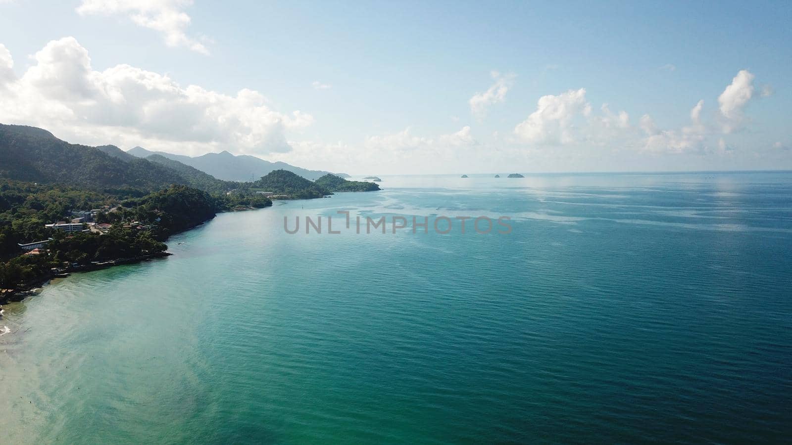 Clear water on the beach of green Chang Island. The turquoise color of the water reflects like a mirror the green hills of the island and the white clouds. Clean sand like in the Maldives. Thailand