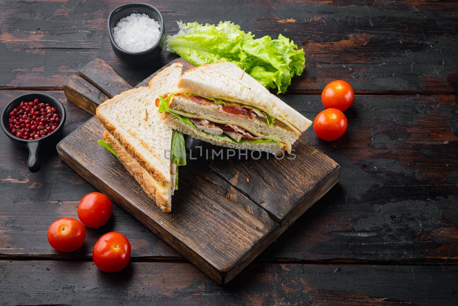 Club sandwich panini with ham, fresh tomato, cheese, on dark wooden background