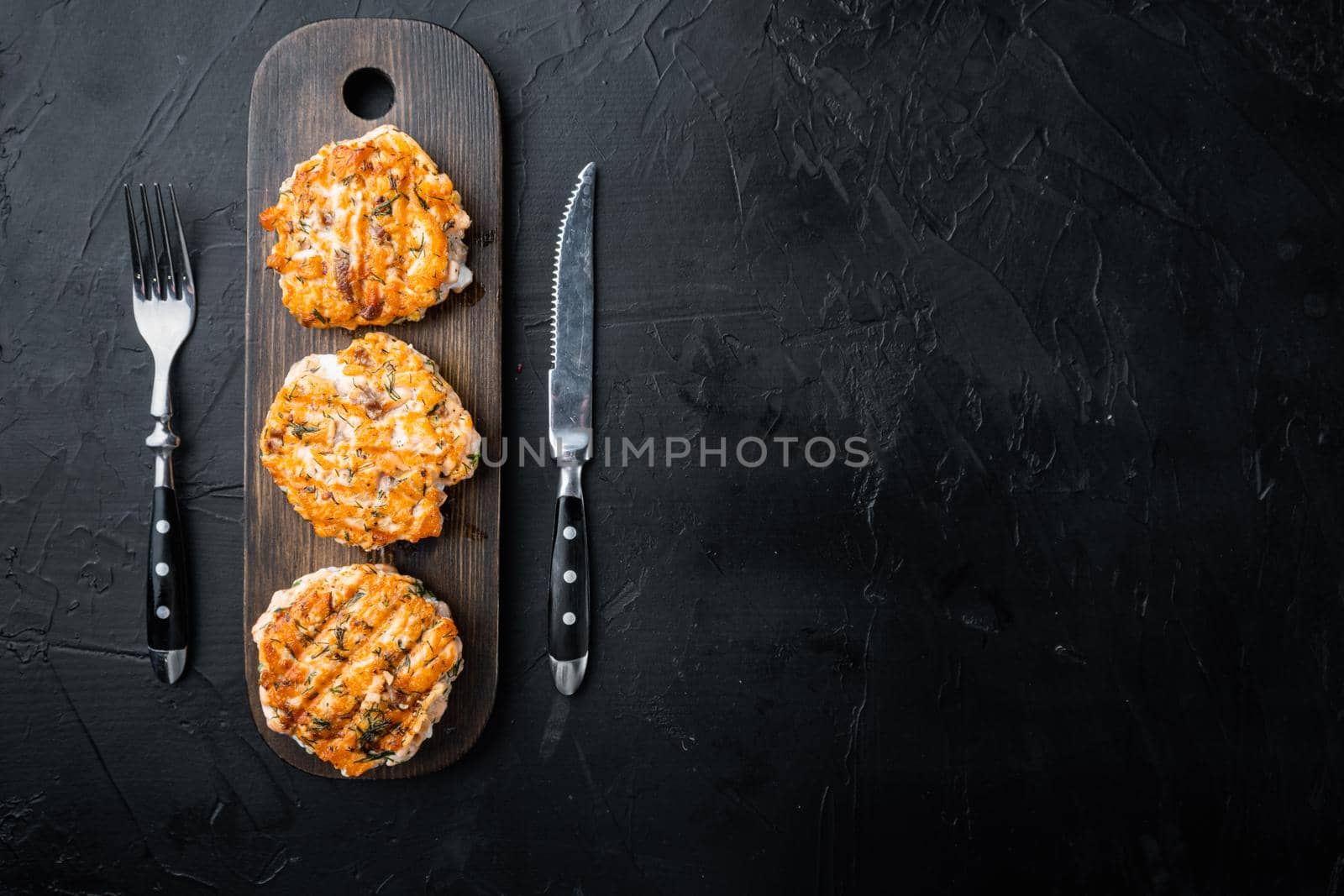 Grilled quick asian fishcakes from salmon and spicy herb, on black textured background, top view with space for text