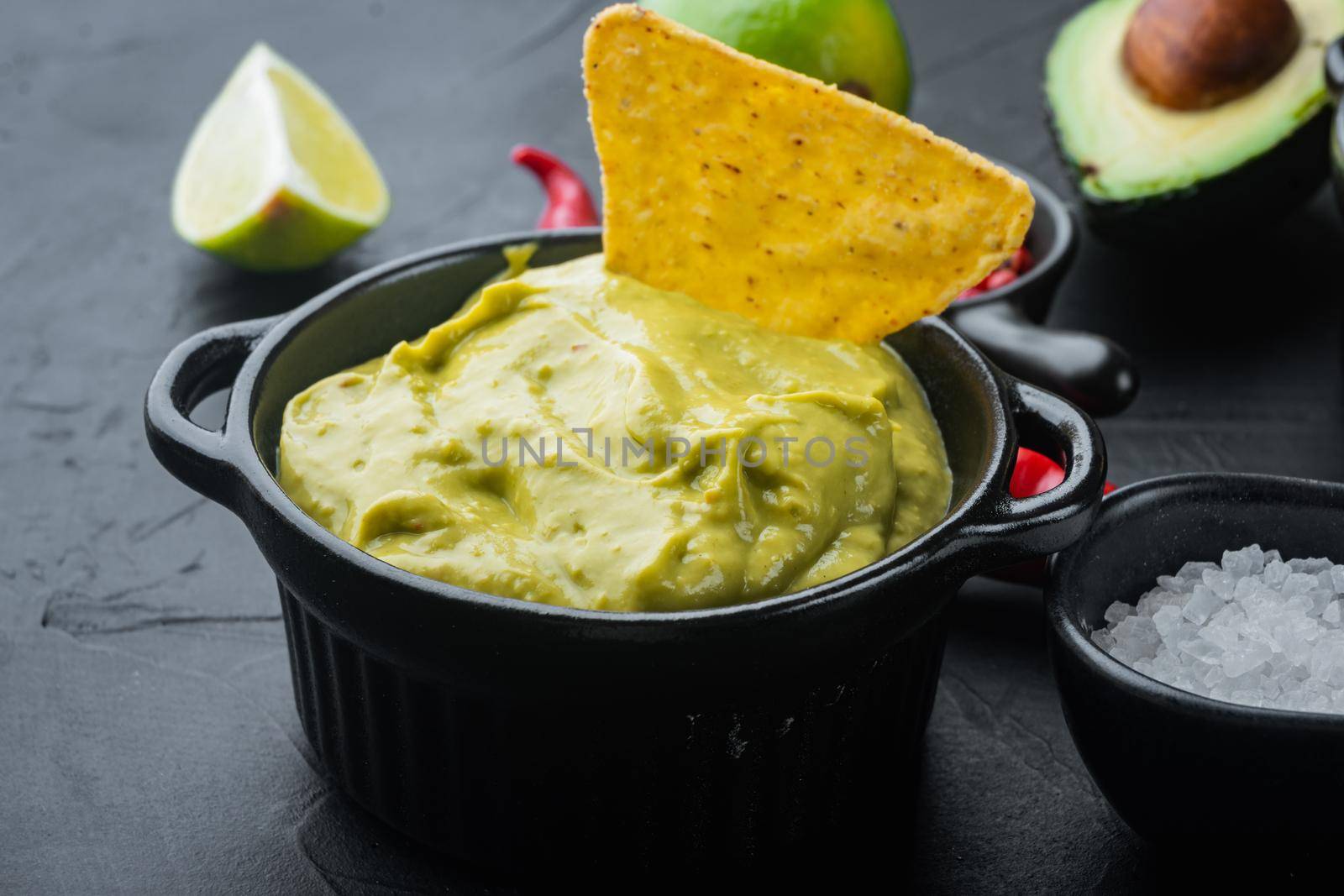 Creamy avocado dip with cilantro and lime in bowl, on black background