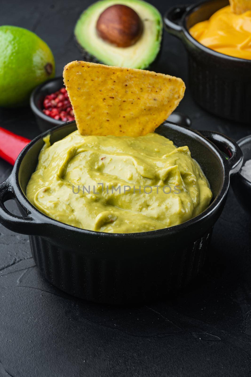 Bowl with guacamole made of ripe avocado, on black background