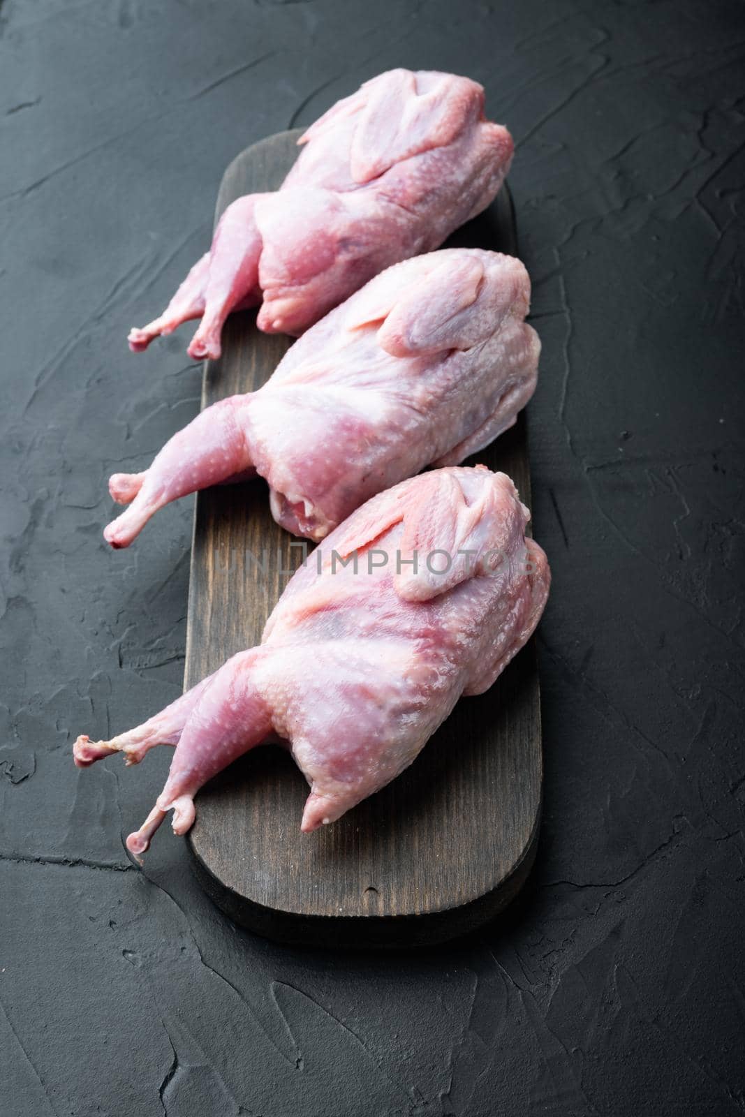 Raw uncooked quails set, on black textured background