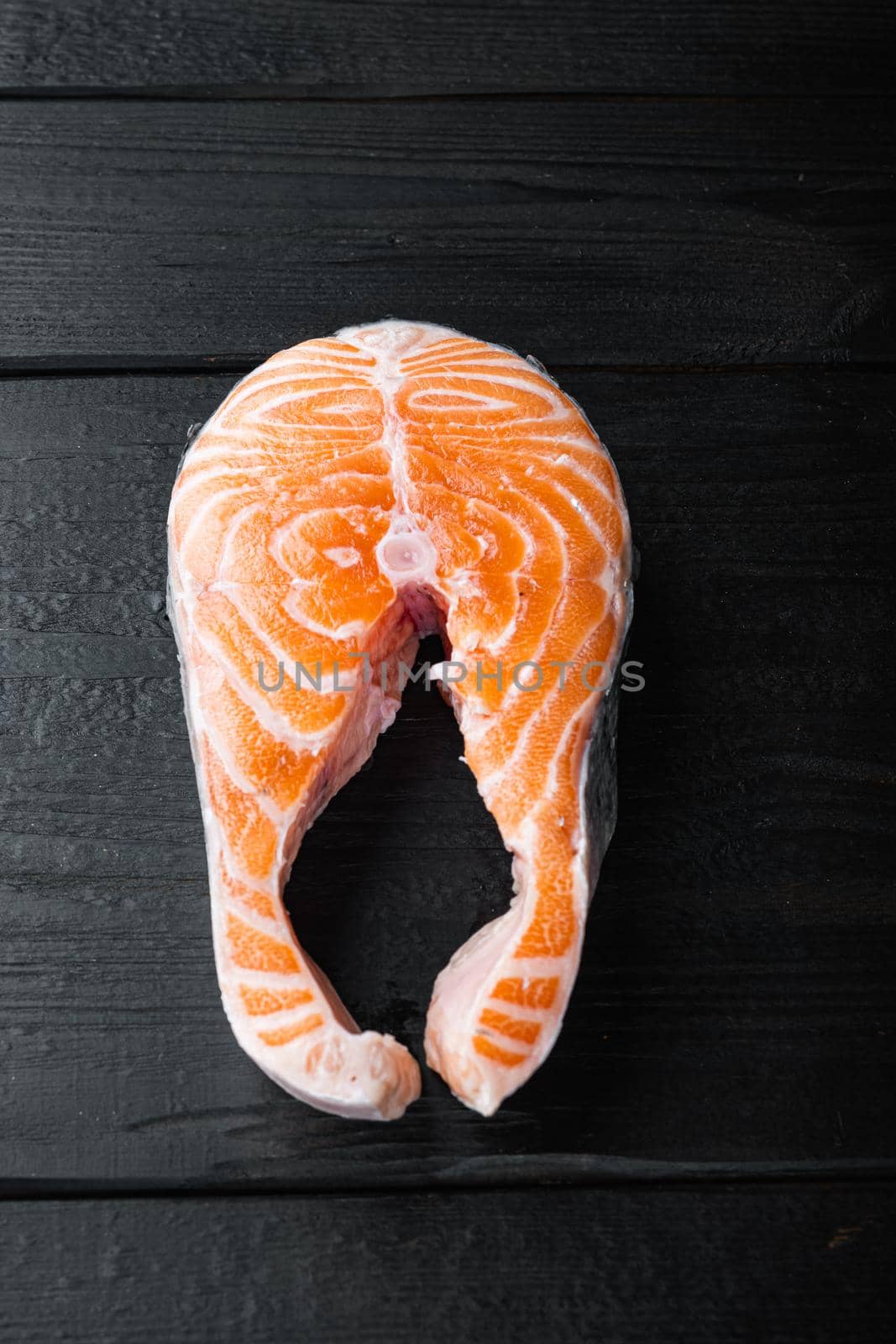 Slice of red fish trout, on black wooden surface, flat view.