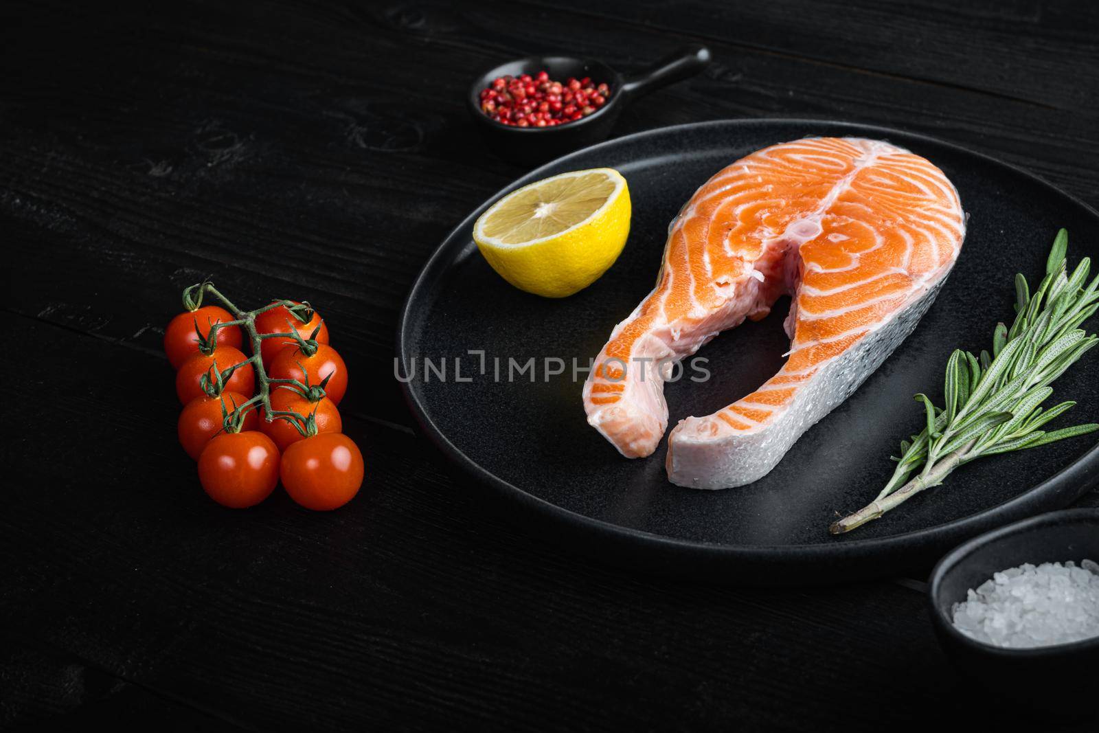 Raw trout steak with herbs, on black wooden surface.