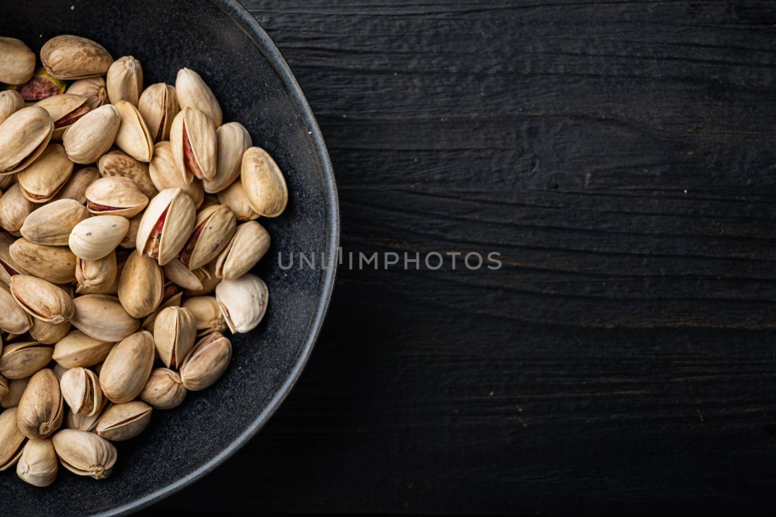 Shelled, unsalted pistachios, on black wooden table, top view with space for text