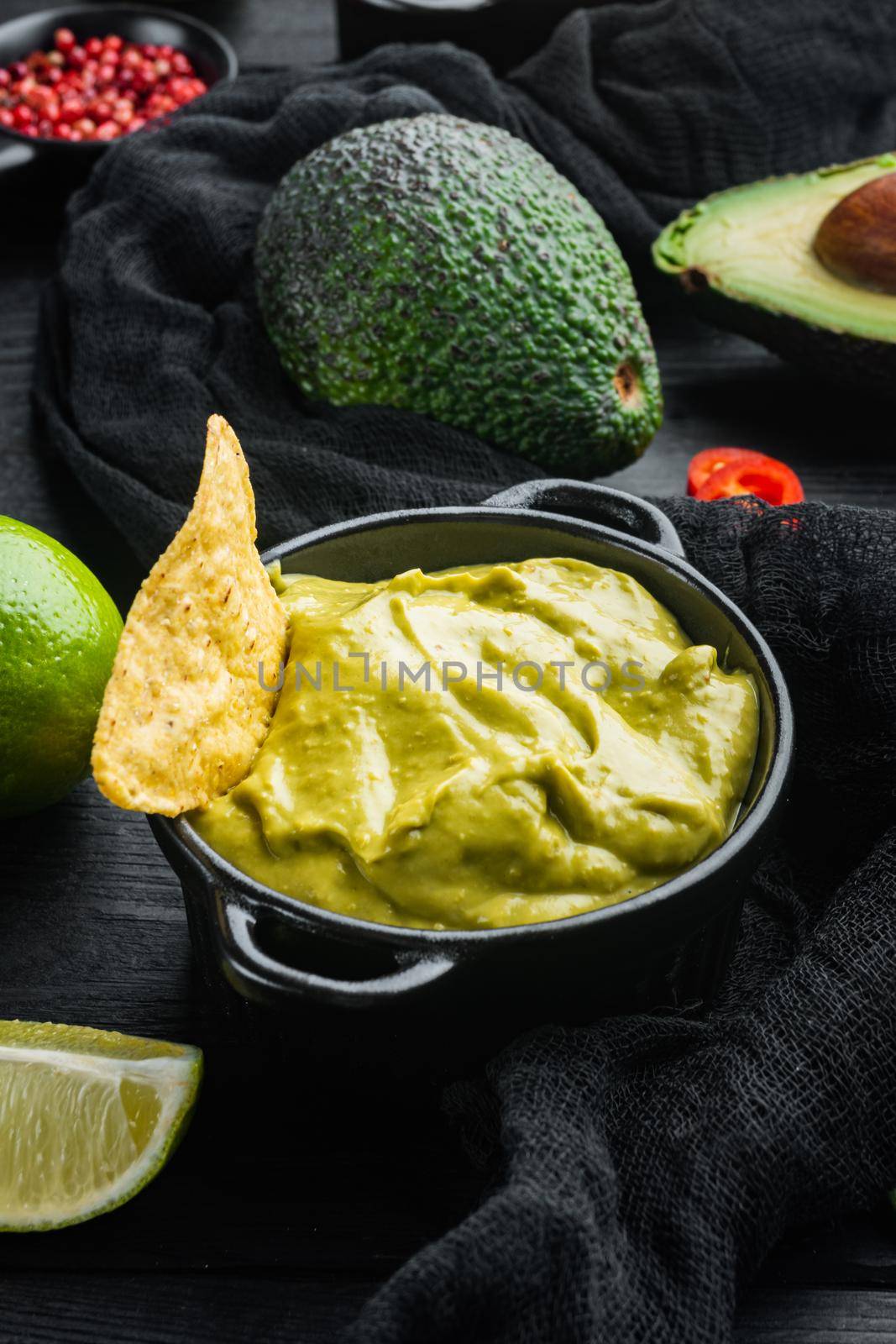 Avocado dip or guacamole in bowl, on black wooden background