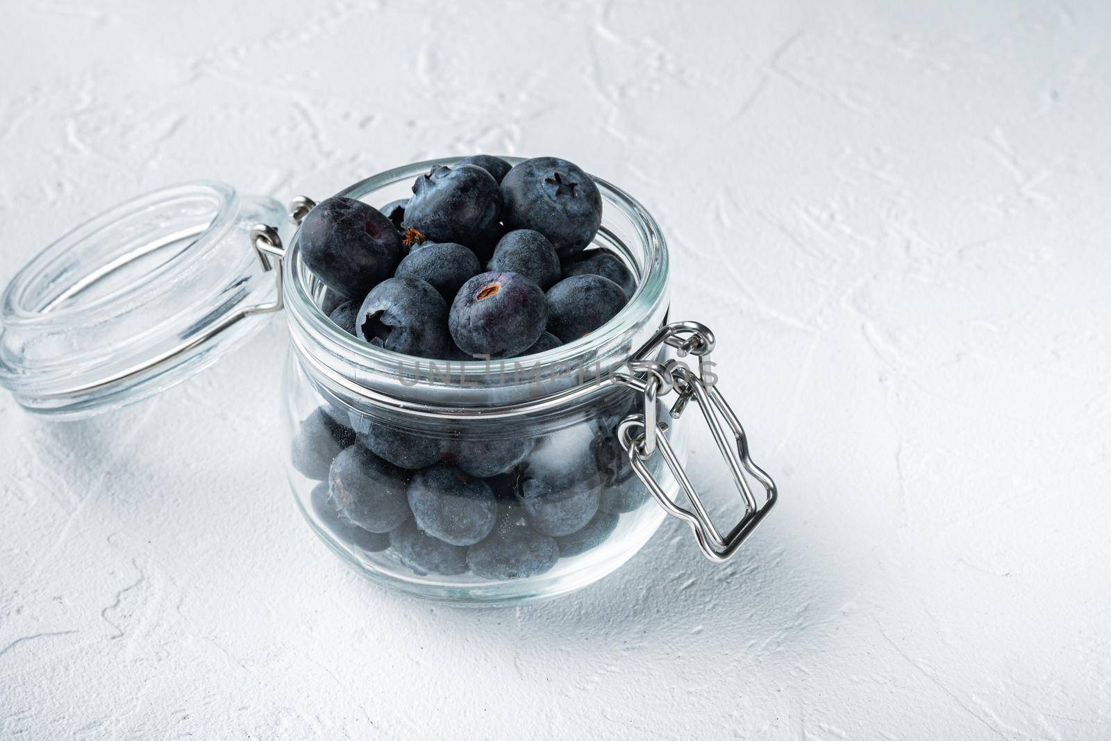 Ripe blueberry in glass jar, on white background.