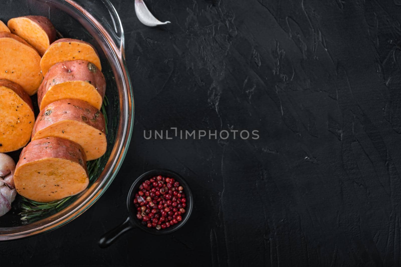 Cajun sweet potatoes for baking with herbs and spices on black background with copyspace.