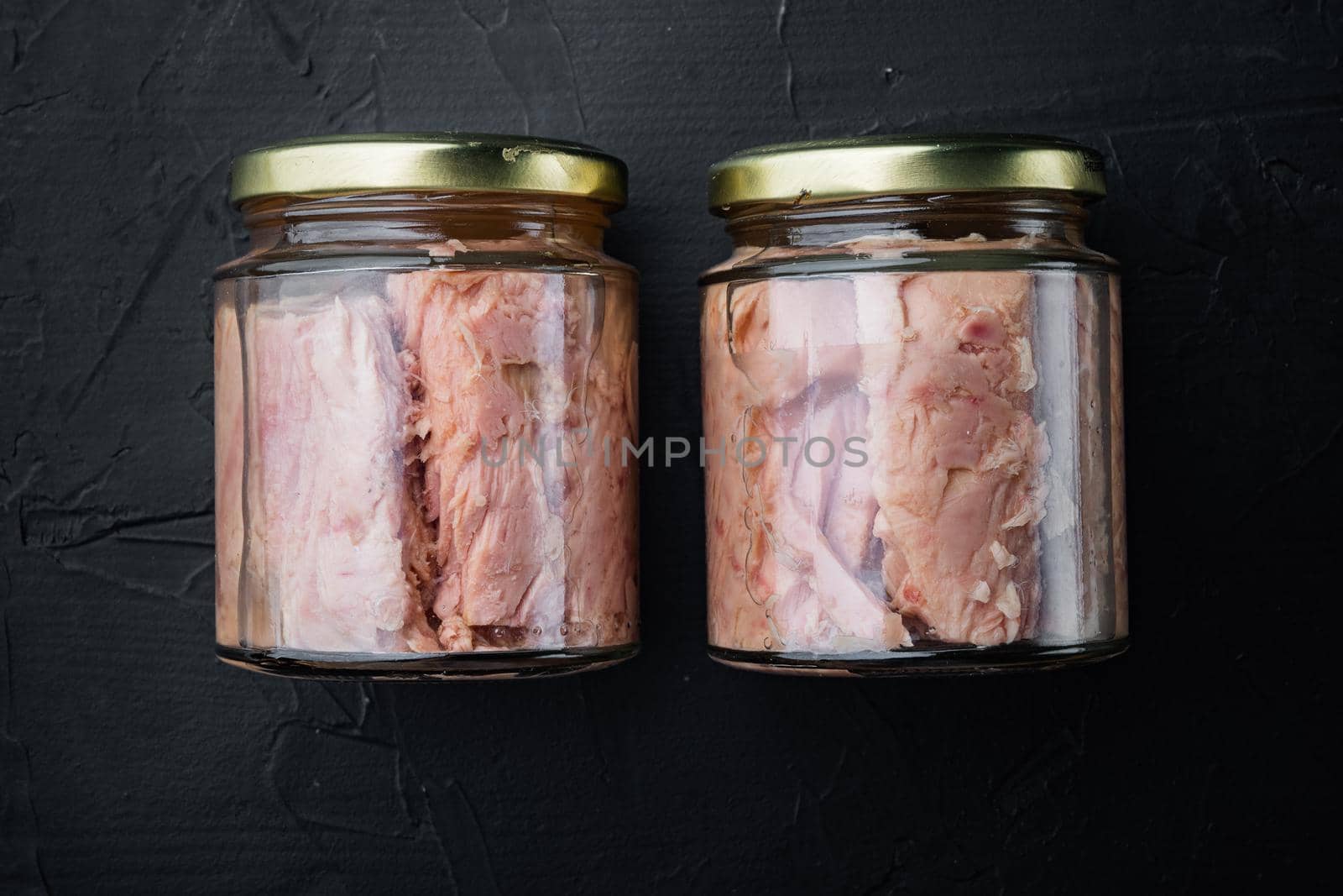 Tuna fillet meat in glass jar, on black background, flat lay