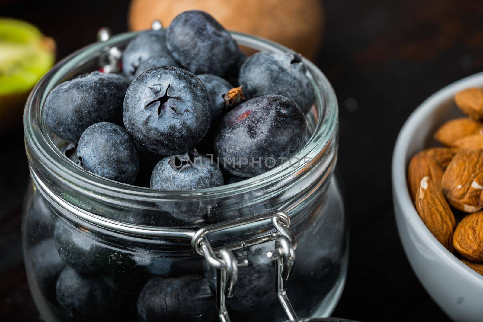 Ripe blueberry in glass jar on dark wooden background.