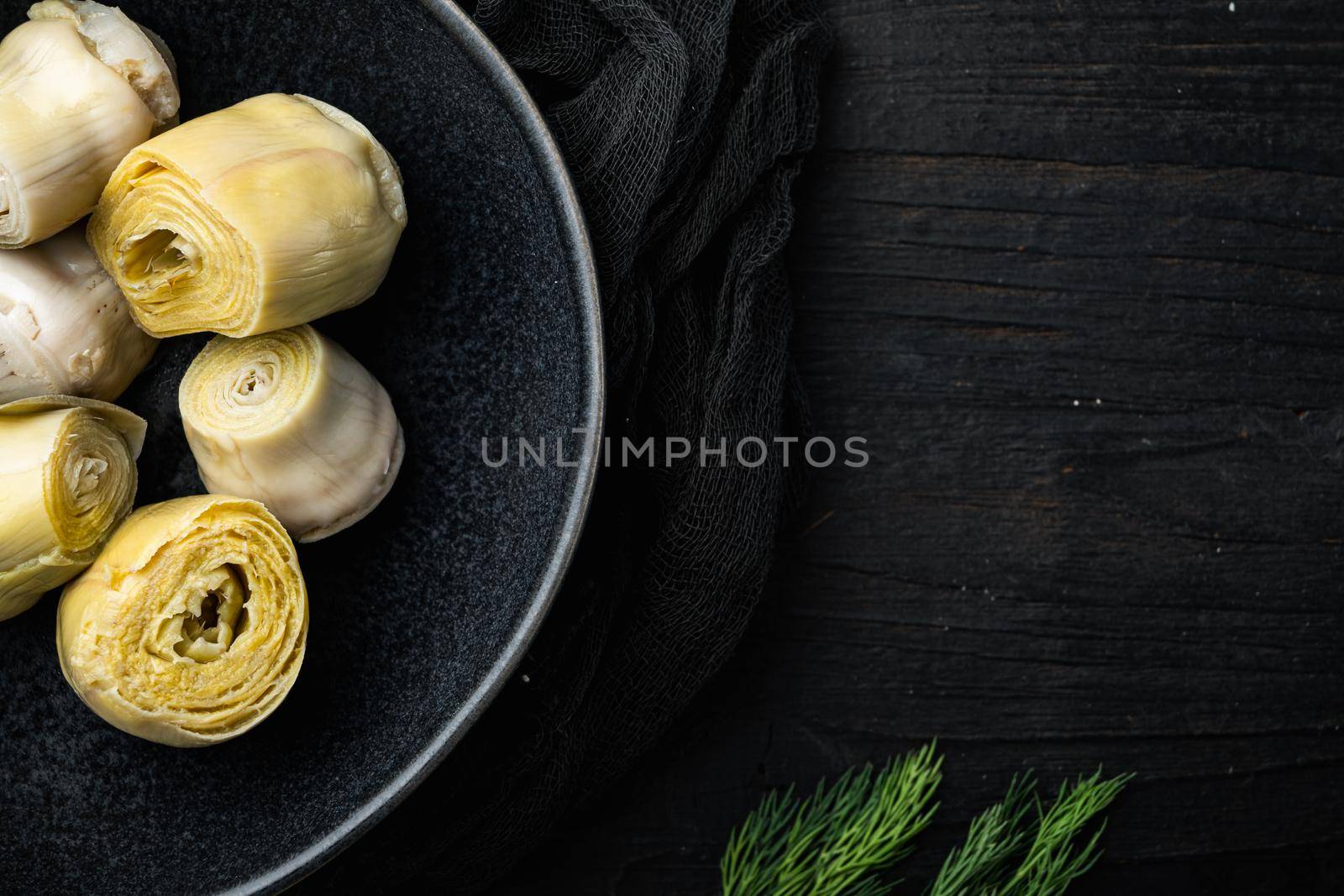 Pickled artichokes with oil, on black wooden table, top view with space for text